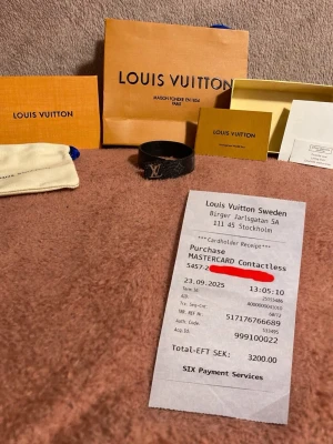 Louis Vuitton svart monogram armband - Snyggt svart armband från Louis Vuitton med klassiskt monogrammönster och guldfärgad LV-logga framtill. Armbandet är tillverkat i läder och har en stilren, rund form. Kommer med originalförpackning, dustbag och certifikat.