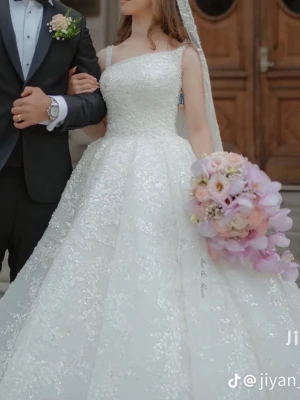 Vit glittrig bröllopsklänning - Drömmig vit bröllopsklänning med glittrande detaljer och bred kjol i prinsessmodell. Klänningen har smala axelband, fyrkantig urringning och är ärmlös. Perfekt för dig som vill känna dig som en prinsessa på din stora dag.