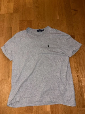 Grå t-shirt från Polo Ralph Lauren - Klassisk ljusgrå t-shirt från Polo Ralph Lauren med liten broderad logga på bröstet. Tillverkad i mjuk bomull och har normal passform. Perfekt basplagg för en enkel och stilren look.
