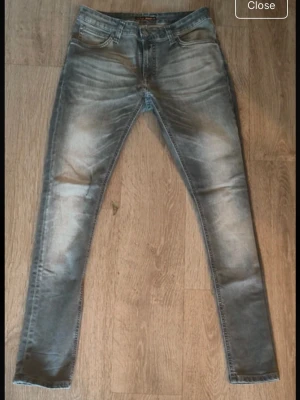 Grå Nudie Jeans - Säljer ett par gråa skinny jeans från Nudie Jeans med slitna detaljer och snygg tvätt. Klassisk femficksmodell med bakfickor som har Nudie-signatur. Jeansen är i stretchigt denim och har en smal passform som sitter tight längs benen.