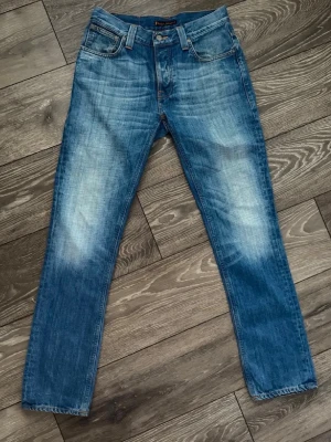 Blå jeans från Nudie Jeans - Snygga blå jeans från Nudie Jeans med klassisk femficksdesign och raka ben. Jeansen har slitningar och ljusare partier framtill samt detaljerade bakfickor med Nudie Jeans signatursöm. Tillverkade i denim av bomull.   OBS beställ med instabox blir mycket lättare för mig skickar samma dag eller dagen efter.