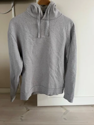 Hoodie från Apc - Snygg ljusgrå hoodie från A.P.C. med minimalistisk design och liten vit logga på bröstet. Hoodien har huva med dragsko och är tillverkad i mjukt material, perfekt för en avslappnad stil.