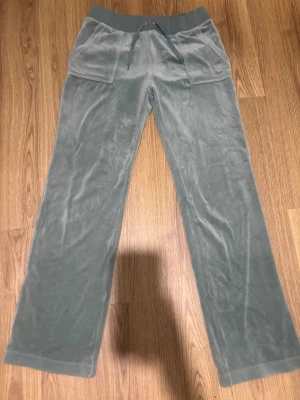 Gröna velourbyxor Juicy Couture - Mysiga mjukisbyxor i ljusgrön velour från Juicy Couture. Byxorna har bred resår i midjan med dragsko, två stora fickor fram och diskret broderad logga på ena fickan. Perfekta för chill dagar och riktigt skön passform. Pris går att diskutera