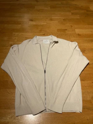 Beige ribbad ziptröja från Jack and jones - Stilren beige ziptröja från jack and jones i ribbstickat material. Tröjan har lång ärm, krage och hel dragkedja framtill. Perfekt för lager-på-lager och enkel att matcha med olika outfits. Öppen för prisförslag!