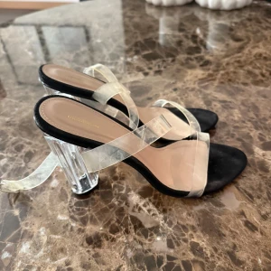 Klara sandaler med transparent klack - Säljer ett par trendiga sandaler från PrettyLittleThing med transparenta remmar och cool klack i akryl-look. Sulan är svart och innersulan beige. Perfekta för dig som vill sticka ut med en modern och stilren vibe.
