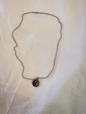 Halsband med yin yang-hänge i stål - Snyggt halsband med kulkedja i silverfärg och ett runt yin yang-hänge i svart och silver. Kedjan är cirka 22 cm lång. Perfekt accessoar för dig som gillar minimalistisk och stilren design med en touch av balans och harmoni.