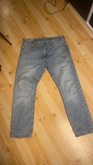 Levi's 551 ljusblå jeans straight fit - Ljusblå Levi's 551 jeans med klassisk straight fit och fem fickor. Jeansen har en snygg tvättad look och ett litet slitet hål på bakfickan för extra karaktär. Perfekt för dig som gillar vintage-vibe och tidlös denimstil.