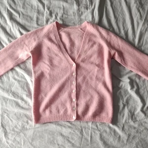 Kashmir kofta med v-ringning - Superfin ljusrosa kashmir kofta med v-ringad hals och vita knappar framtill. Mjuk och skön känsla, perfekt att slänga på sig när det är lite kyligt. Långärmad och med ribbade muddar vid ärmslut och nederkant. Enkel och stilren design.