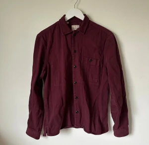 Vinröd skjorta från Selected Homme - Snygg vinröd skjorta från Selected Homme i 100% ekologisk bomull. Klassisk modell med lång ärm, bröstficka och svarta knappar framtill. Perfekt för dig som gillar stilrena och enkla plagg med en modern touch. 4Ö10