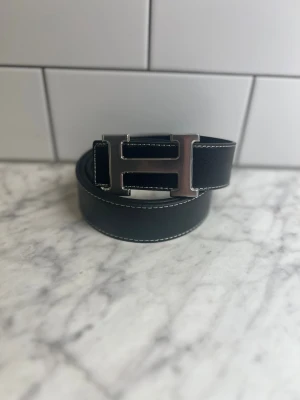 Bälte - Svart läderbälte med silverfärgat H-spänne  Helt nytt bälte i svart läder med stilrent silverfärgat H-format spänne ✨ Klassiskt, elegant och passar till allt. Perfekt för både vardag och fest. 📦 Skickas snabbt och tryggt! 