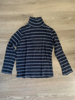 Randig polotröja från Power Boys - Mörkblå polotröja med vita och blå ränder från Power Boys. Tröjan har lång ärm och klassisk polokrage, perfekt för dig som gillar enkel och stilren design. Materialet är mjukt och skönt, passar dig som vill ha en chill look.