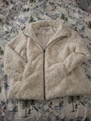 Vit teddyjacka från Stories  - Mysig teddyjacka i vit färg från Stories, storlek M. Jackan har fluffig pälslook, hög krage och hel dragkedja framtill. Perfekt för kalla dagar. Passformen är normal och jackan har långa ärmar.