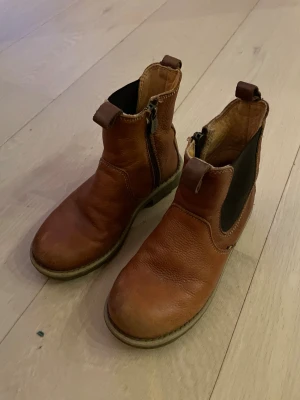 Bruna skinnboots från Kavat - Snygga bruna boots från Kavat i äkta skinn med dragkedja på sidan och elastisk panel. De har rund tå, platt sula och praktisk ögla bak för enkel påtagning. Perfekta för höst och vinter, passar till många olika outfits.