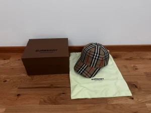 Burberry keps - Snygg keps från Burberry med det ikoniska rutiga mönstret i beige, svart, vitt och rött. Justerbar baktill med Burberry-logga. Perfekt accessoar för dig som vill ha en lyxig och trendig look. Kepsen kommer med originalförpackning och dustbag.         Pris kan alltid diskuteras 