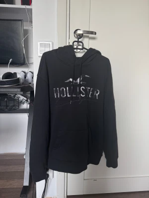 Svart Hollister hoodie med logga - Svart hoodie från Hollister i storlek S med stor broderad logga och text på bröstet med snörning. Riktigt snygg sällsynt tröja med riktigt bra kvalité 