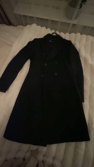 Svart kappa från Zara XS - Stilren svart kappa från Zara i klassisk modell med dubbelknäppning och lång ärm. Snygg  och tidlös design. Säljs pågrund av att den är för liten. Fråga om bilder så kan jag skicka. 