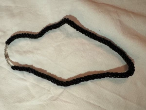 Svart tvinnat pärlhalsband - Unikt halsband med tvinnad design av små svarta pärlor och transparenta pärlor vid låset. Halsbandet är ca 50 cm långt och har ett metallspänne. Perfekt för dig som gillar statement-smycken med lite edge.