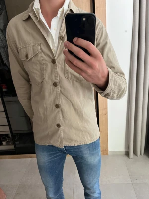 Beige overshirt från Uniqlo - Säljer en beige overshirt från Uniqlo i storlek M i väldigt bra skick!                                                          ———————————————————————————- 📐| Storlek: M                                                          👖| Märke: Uniqlo                                                     🔎 | Skick: 9/10                                                        ✍🏻 | Skriv om du har några frågor