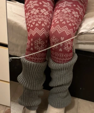 gråa vintermönster/benvärmare - Säljer ett par röda leggings med vita snöflingor, hjärtan och zigzag-mönster. Perfekta för vintermys! Materialet är mjukt och stretchigt, och de har en tajt passform. Färgen är röd med vita detaljer. Stickade grå benvärmare ingår ej.