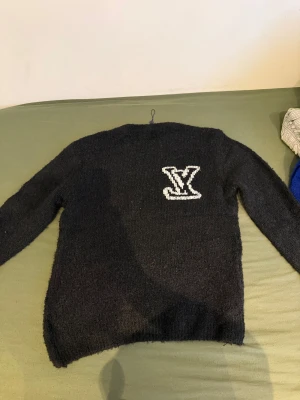 Louis Vuitton stickad tröja med LV-logga - Snygg stickad tröja från Louis Vuitton med stor LV-logga på bröstet. Finns i både svart och klarblå färg. Tröjan har rund hals och långa ärmar, perfekt för dig som vill ha en lyxig och trendig look. Materialet är mjukt och fluffigt stickat.