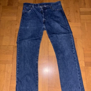 Levi's 501 blå jeans W36 L32 - Klassiska blå Levi's 501 jeans med rak passform och knappgylf. Jeansen har fem fickor och är tillverkade i slitstarkt denim. Perfekta för dig som gillar tidlös stil och vill ha ett par ikoniska jeans i garderoben.