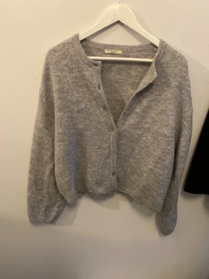 Grå kofta från gina - Mysig grå kofta från gina. Tröjan är stickad i mjukt material och har en loose passform med långa ärmar. Perfekt för lager-på-lager och chill dagar.