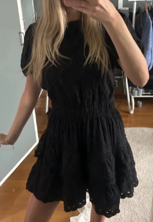 Svart kort klänning från Zara  - Supersöt svart kort klänning med puffärmar och markerad midja. Kjolen har volanger och broderade detaljer längst ner. Perfekt för dig som gillar en feminin och trendig stil.