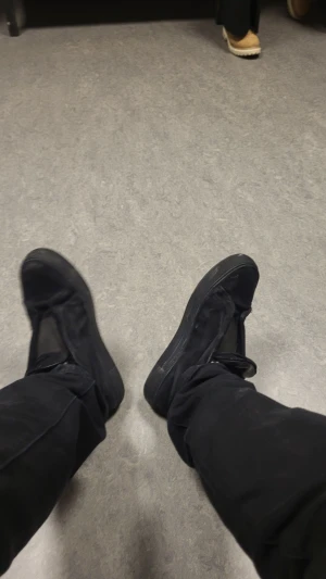 Arigatos (Buda) - Säljer ett par helsvarta sneakers med platt sula och rund tå. Skorna har klassisk snörning och är tillverkade i ett syntetmaterial med tygdetaljer. Perfekta för dig som gillar en clean och enkel stil.