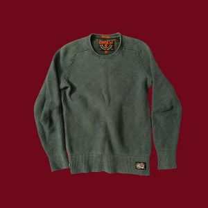 Grön stickad tröja från Superdry - Snygg grön stickad tröja från Superdry i storlek S. Tröjan har rund hals och ett diskret Superdry-märke vid nederkanten. 