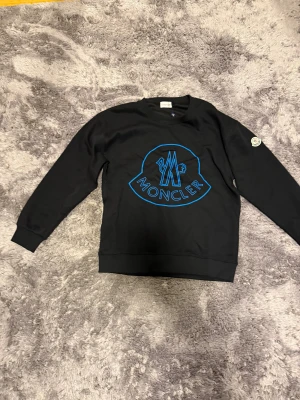  Moncler sweatshirt  - Svart sweatshirt från Moncler med stort blått logotryck på bröstet och klassisk rund hals.(liten i storlek) PRIS KAN DISKUTERAS 
