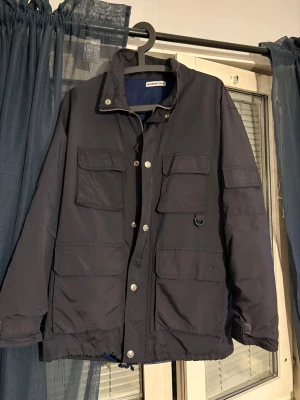 vindjacka från valentino - Svart vindjacka med fyra stora fickor framtill, dragkedja med tryckknappar. Jackan har en clean look och är perfekt för dig som gillar praktiska detaljer och stilren design.