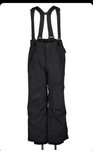 Svarta täckbyxor/skidbyxor med hängslen - Svarta täckbyxor med justerbara hängslen och bred passform Från Everest. Byxorna har dragkedjor vid fickorna och reflexdetalj på ena benet. Perfekta för kalla dagar och vinteraktiviteter. Köpte för 600kr