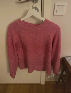 Rosa stickad tröja från Vero Moda - Mysig rosa stickad tröja från Vero Moda i storlek S. Tröjan har en rund halsringning och långa ärmar med ribbade muddar vid hals, ärmslut och nederkant. Perfekt för att hålla värmen under kyliga dagar och har en enkel, klassisk look.