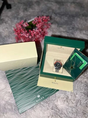 Rolle Submariner svart/röd stål - Rolle Submariner med svart urtavla och röd-svart vridring. Klockan har en klassisk rund form och länkarmband i blankt stål. Levereras i originalbox med certifikat och tillbehör. En ikonisk och stilren klocka för dig som gillar exklusiva accessoarer.