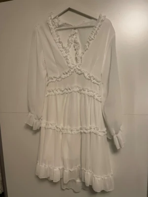 Vit kort klänning med volanger - Supersöt vit klänning med volanger och v-ringning, långärmad med öppen rygg. 