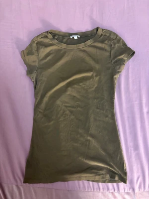 Olivgrön t-shirt från Massimo Dutti - Säljer en enkel olivgrön t-shirt från Massimo Dutti i storlek S. T-shirten har rund hals och korta ärmar, tillverkad i mjuk bomull som känns skön mot huden. Perfekt för dig som gillar stilrena och neutrala plagg.