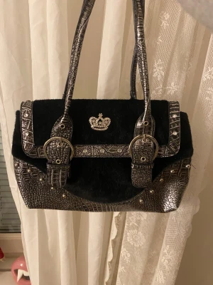 Svart och silver handväska - Säljer en Unik handväska i svart pälsimitation med silverfärgade detaljer i krokopräglat skinn💕Väskan har nitar samt en glittrande krona framtill. Perfekt för dig som gillar statement-accessoarer och coola detaljer.🌹🌹