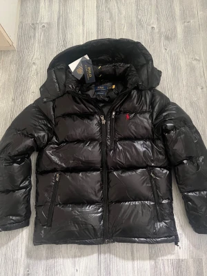 Ralph Lauren jacka - Hej! En glossy Ralph lauren jacka till salu. Jackan är i jättebra skick och den har inga defekter elller tecken av användning. Jackan är köpt på Nk och kvittot finns kvar. Jag säljer jackan pågrund av att den tyvärr inte passar mig, priset kan diskuteras lite vid snabbaffär. hör av dig vid frågor 😁