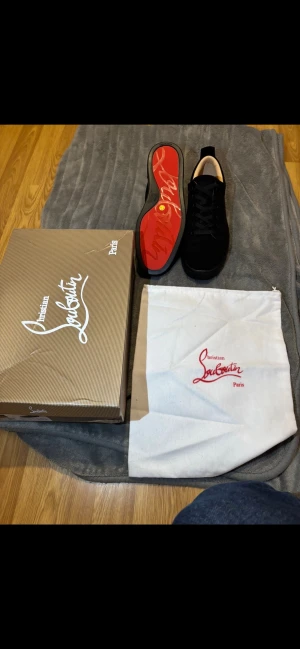 Christian Louboutin svarta sneakers - Svarta sneakers från Christian Louboutin med klassisk röd sula och guldfärgad logga på innersulan. Skorna har rund tå, snörning och är tillverkade i mocka med beige insida. Medföljer originalkartong och dustbag. Pris kan diskuteras vid ett snabbt köp