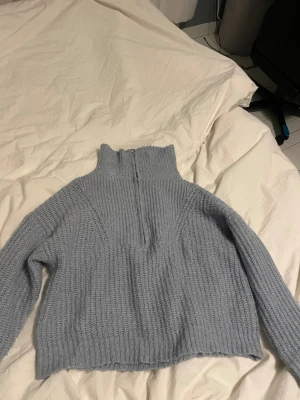 Ljusblå stickad tröja med half zip - Mysig ljusblå stickad tröja från ONLY med hög krage och half zip-dragkedja med metallring. Tröjan har grov ribbstickning och långa ärmar, perfekt för kyliga dagar. Snygg och enkel att matcha med jeans eller kjol.