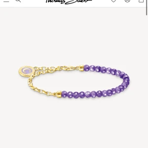 Lila pärlarmband från Thomas Sabo - Snyggt armband med facetterade lila pärlor och guldfärgade detaljer från Thomas Sabo. Armbandet har en tunn kedja och en rund berlock med lila och guld. Perfekt för dig som gillar färg och stilrena smycken.