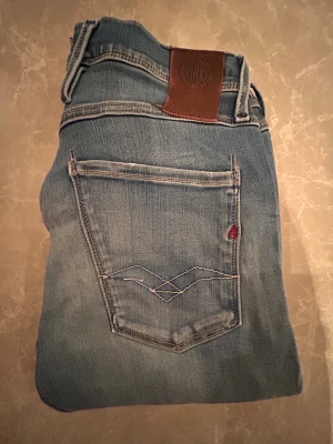 Replay anbass  - Säljer ett par snygga blå jeansshorts från Replay med klassisk femficksmodell och coola slitningar framtill. Shortsen har en brun läderpatch bak i midjan och kontrastsömmar på bakfickorna. Perfekta för en avslappnad streetstil.