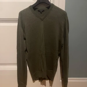 Grön stickad tröja Paul & friends L - Mörkgrön stickad tröja från Paul & friends i storlek L, passar M. Tröjan har v-ringad hals och långa ärmar med ribbade muddar vid hals, ärmslut och nederkant. Perfekt för dig som gillar enkel och stilren design. Pris kan diskuteras!