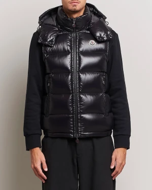 Moncler väst  - Snygg svart dunväst från Moncler med glansig finish och ikonisk logga på bröstet. Västen har en quiltad design, hög krage och dragkedja framtill. Perfekt att slänga över en hoodie för extra värme. Stilsäker och tidlös look.