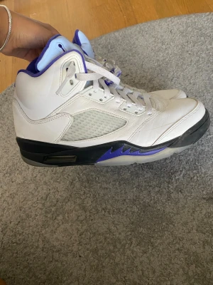 Nike Air Jordan 5 vit/lila sneakers - Säljer ett par Nike Air Jordan 5 sneakers i vitt skinn med lila detaljer och svart sula. Skorna har klassisk snörning, meshpaneler på sidorna och ikonisk Jumpman-logga på plösen.  säljer då dom e för stora 💔