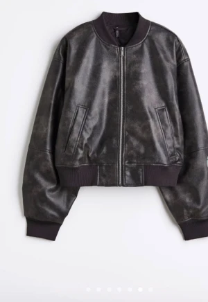 Svart skinn bomberjacka från H&M - Säljer en svart bomberjacka i skinn från H&M med cool vintage-look. Jackan har ribbade muddar, dragkedja framtill och två snedställda fickor. Modellen är loose fit och har långärmade ärmar. Perfekt för dig som vill ha en edgy stil.