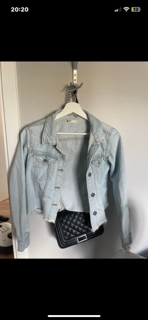 Ljusblå croppad jeansjacka Gina Tricot - Säljer en ljusblå croppad jeansjacka från Gina Tricot med rå kant nertill och klassiska knappar framtill. Jackan har två bröstfickor med lock och långa ärmar. Perfekt för dig som gillar en trendig och avslappnad stil.