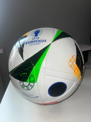 UEFA Euro 2024 fotboll  - Säljer en officiell UEFA Euro 2024 FUSSBALLLIEBE fotboll från Adidas. Bollen är vit med coola detaljer i svart, grön, gul, blå och orange. Den har ett grafiskt mönster och är tillverkad i slitstark syntetmaterial, perfekt för matcher och träning.