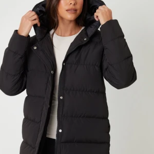 Svart pufferjacka med huva - Säljer en svart pufferjacka med huva och dragkedja framtill. Jackan har en loose passform och är quiltad med breda kanaler. Perfekt för kalla dagar och har praktiska sidofickor. Stängs med både dragkedja och tryckknappar. Stilren och enkel design.