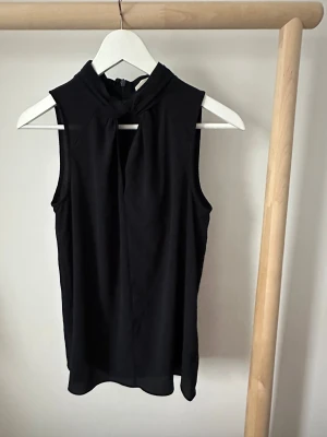 Mörkblå ärmlös blus Michael Kors XS - Mörkblå blus från Michael Kors i storlek XS. Snygg hög hals med knyt-detalj framtill och dragkedja i ryggen. Ärmlös och lätt flowy passform, perfekt till jeans eller kjol. 